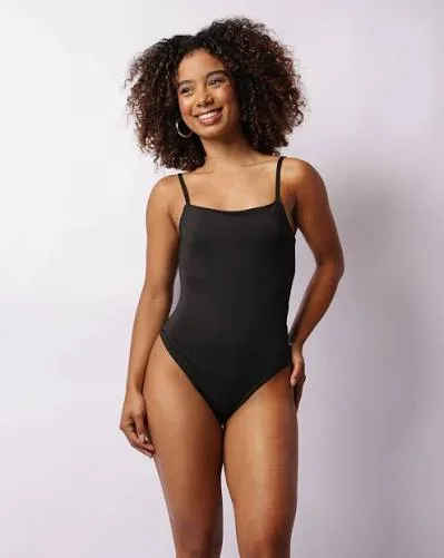 Mulher sorrindo, vestindo body preto liso de alça fina.