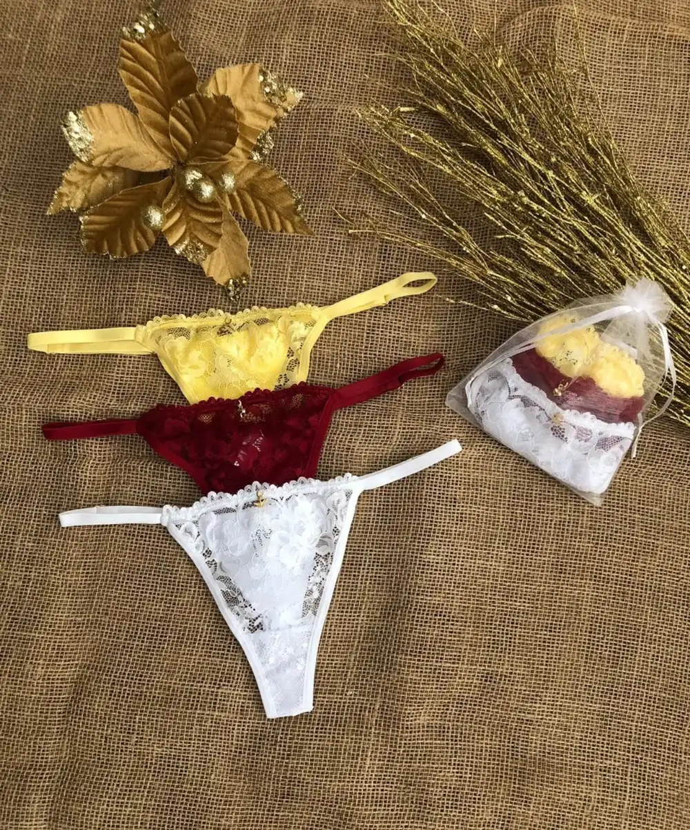 Três calcinhas em renda nas cores amarela, vinho e branca, ao lado de um saquinho de organza.