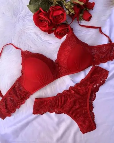 Conjunto de sutiã e calcinha vermelhos em renda, ao lado de rosas vermelhas.