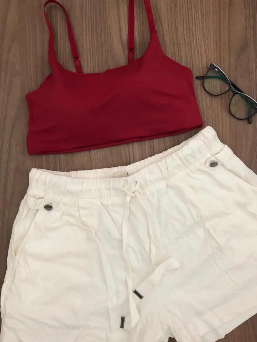 Top vermelho de alça fina combinado com short branco e óculos.